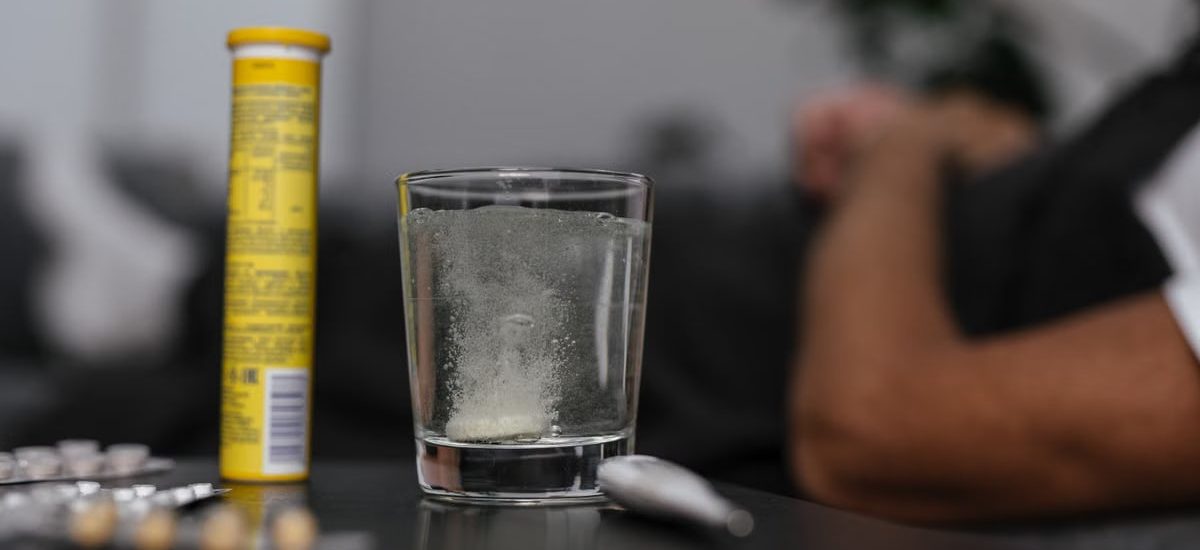 Effervescent tablet dissolving in glass, surrounded by medications, provides a healthcare-focused scene.